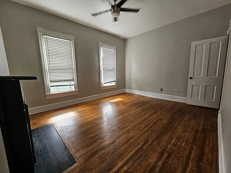 A large master bedroom with high ceiling and rustic wooden flooring. Two large windows that offer street view and plenty of sunlight during the day.