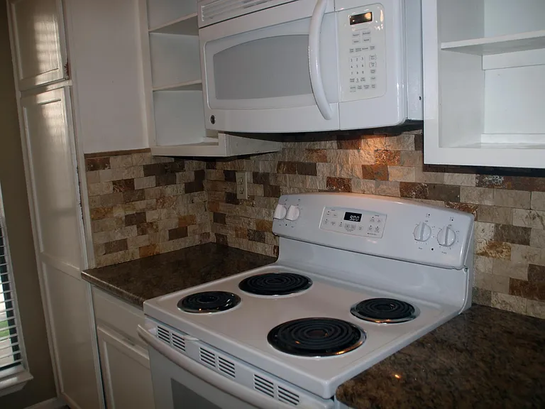 Full size electric range and over-range microwave, granite counter tops, and imported stone backsplash
