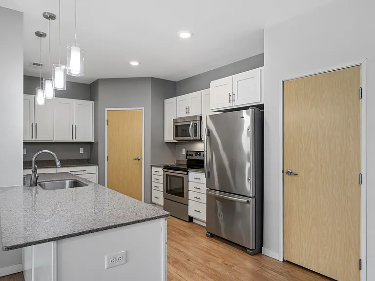 Modern kitchen with sleek stainless steel appliances, elegant white cabinets, and granite countertops under stylish pendant lighting. Modern kitchen with sleek stainless steel appliances, elegant white cabinets, and granite countertops under stylish penda