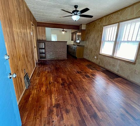 View of living room, from inside front door. Brick partial wall at end of room is the divider wall between kitchen and living room. Glass top electric stove is behind the brick partial wall.