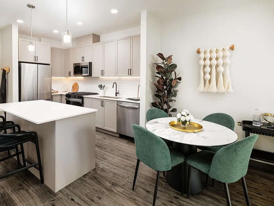 Kitchen and dining area with grey cabinetry, white quartz countertops, white tile backsplash, stainless steel appliances, and pendant lighting