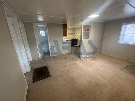 Living room with front windown and entry. Kitchen top left.