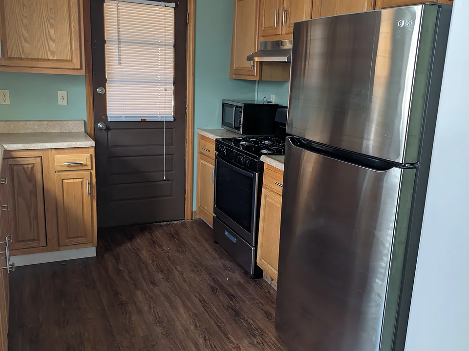 Kitchen view with SS refrigerator, range, range hood. Oak cabinets, formica counter, laminate floor. Door leads to enclosed back porch. Kitchen size: 9 x 11