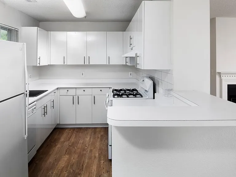 Wilmington Classic Package kitchen with white cabinetry and appliances, white or beige laminate countertops, and white tile backsplash. Select homes include stainless steel appliances, hard surface plank flooring in common areas, and kitchen islands