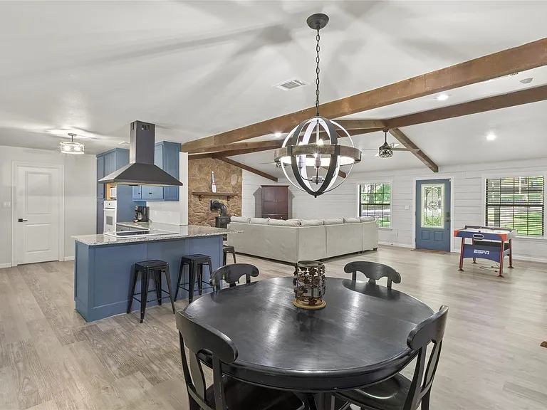 Open-concept living space with vaulted ceilings, exposed wood beams, wood-finish flooring, a kitchen island with stone countertop, and a stone accent wall