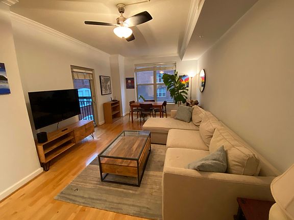 Hardwood floor living room with L-shaped West Elm couch, coffee and end tables, ceiling fan, and a wall-mounted television.