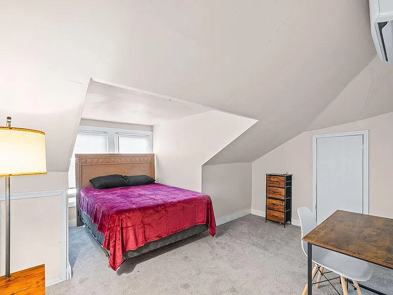 Furnished bedroom with a full bed, desk area, dresser storage, and two windows plus a sloped ceiling for added character.