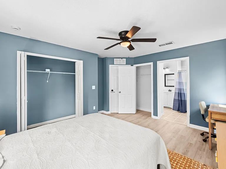 Spacious bedroom with ceiling fan, wood-look flooring, two closets, and convenient access to the ensuite bathroom.