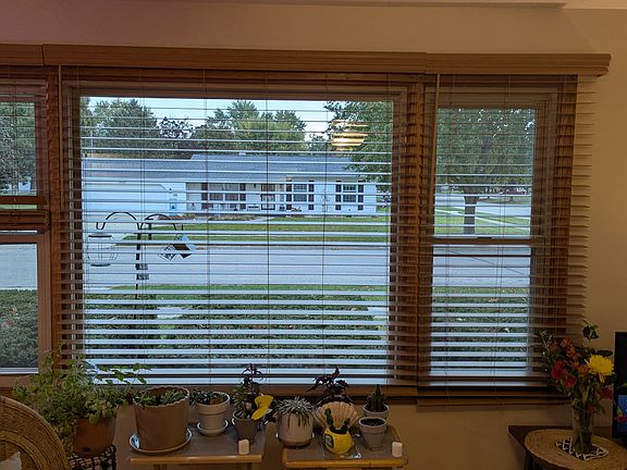 Across quartz counter with lower cabinets out large front window with wooden blinds.