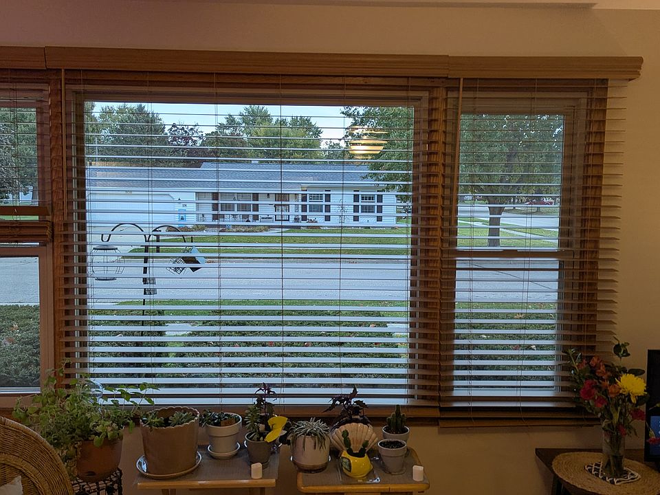 Across quartz counter with lower cabinets out large front window with wooden blinds.