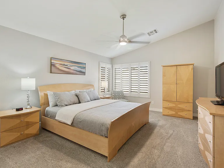 Primary bedroom with King size bed, 2 nightstands, armoire, dresser, fan, chair, tv and entrance to ensuite
