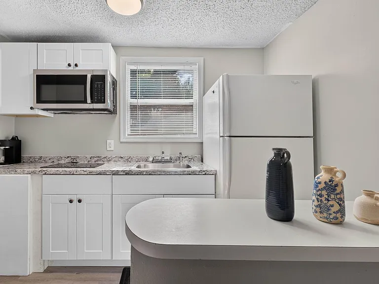 Compact kitchen with ample white cabinetry, laminate counters, sink with window view, and full-size fridge plus microwave.