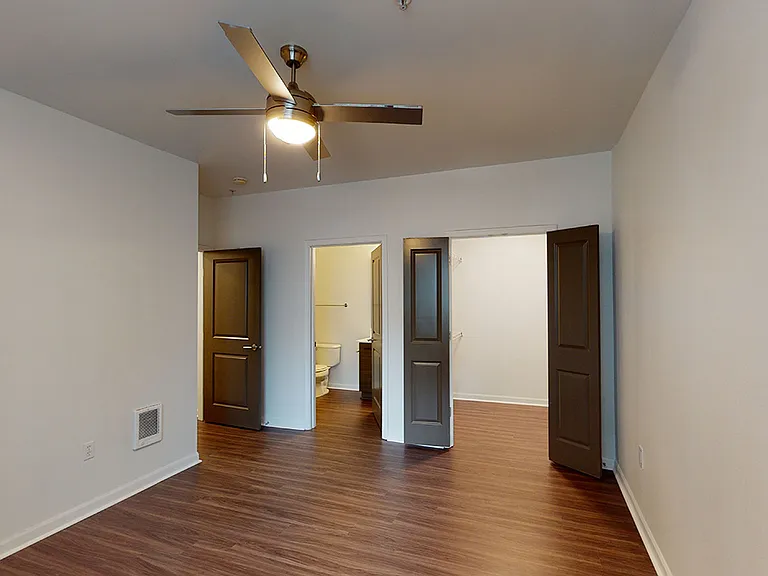 Spacious apartment bedroom with large closet, attached bathroom and wood-style flooring.