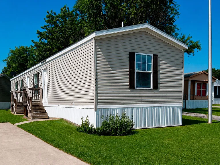Exterior view of the manufactured home at Winterbrook Lot 349 in Greenwood, Indiana. Features blue siding, a welcoming entry with wooden steps and railings, and a well-maintained lawn within the Winterbrook community.