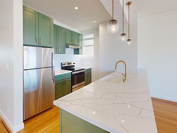 Kitchen with multiple cabinets, refrigerator, stove, range hood, and sink