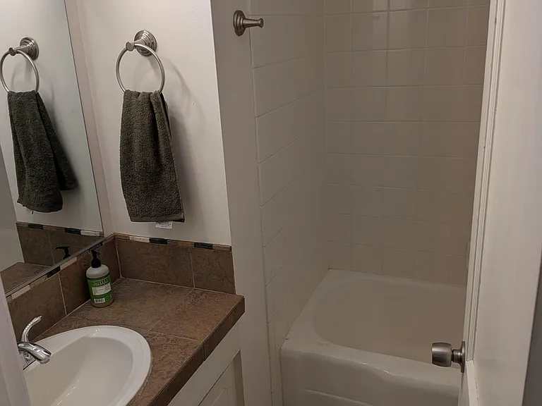 Full bathroom with a tiled tub/shower combo, vanity with counter space, and wall mirror for daily convenience.