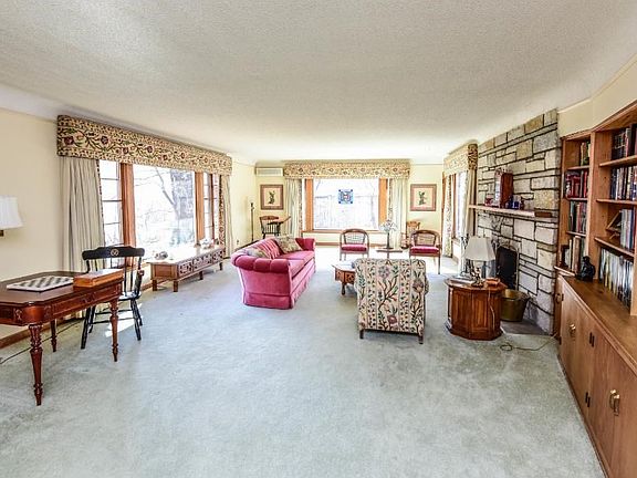 Main level living room with an area for your own personal library, wood burning fireplace and beautiful windows that overlook this gorgeous yard.