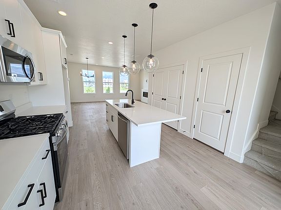 Modern kitchen with white cabinets, stainless steel appliances, a central island with sink, pendant