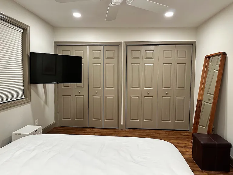 Two closets with custom storage organizers and a mounted, adjustable smart TV.