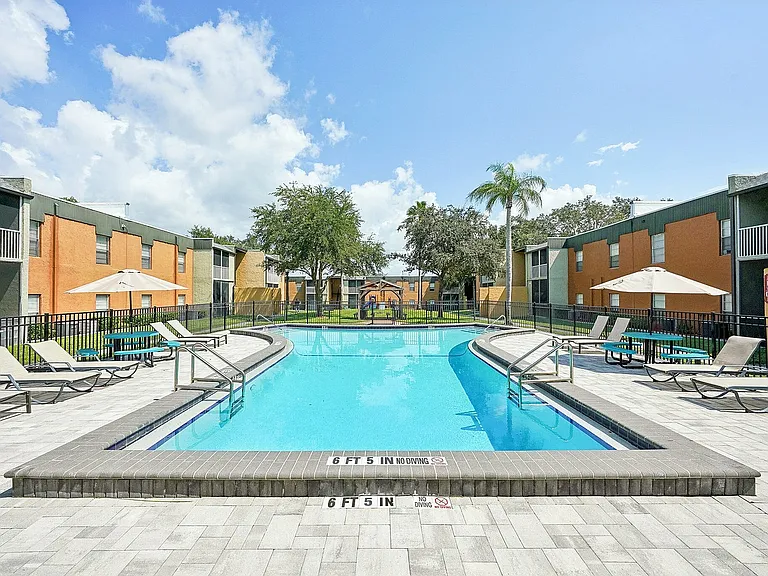 Inviting apartment community courtyard featuring a pristine swimming pool surrounded by sun loungers and lush greenery.