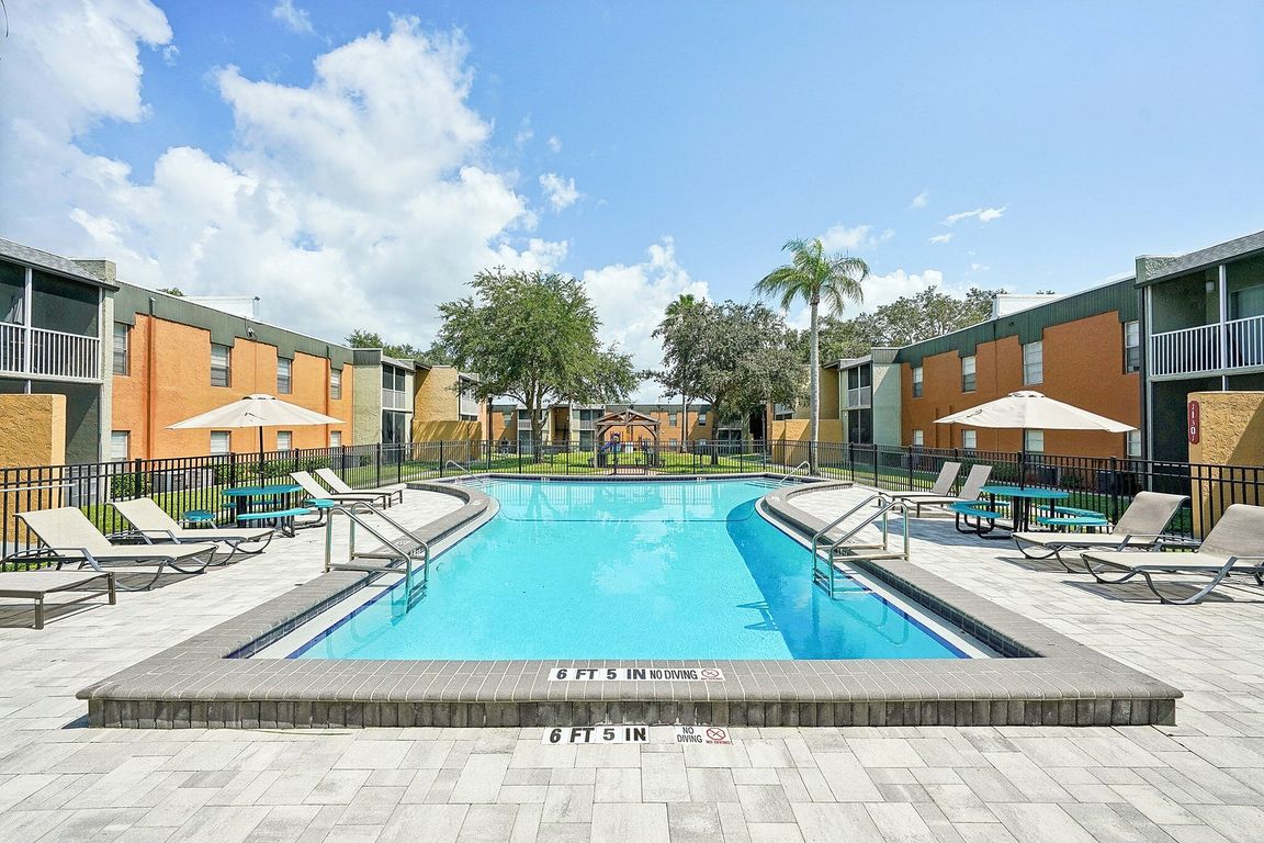 Inviting apartment community courtyard featuring a pristine swimming pool surrounded by sun loungers and lush greenery.