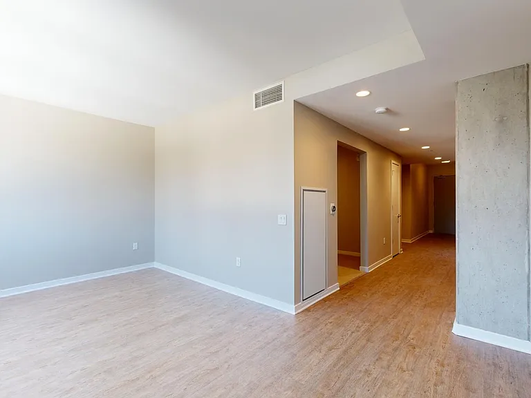 Apartment kitchen with stainless steel appliances, dining and living room with wood-style flooring.