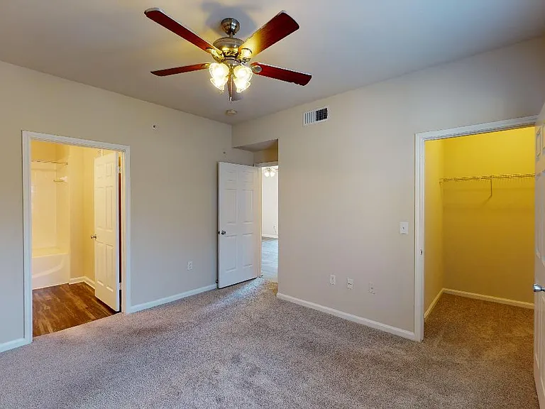 Spacious apartment bedroom with large closet, attached bathroom and plush carpet flooring.