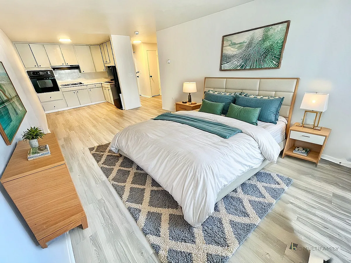 Inviting apartment interior showcasing a bright bedroom with elegant wooden furniture and a cozy kitchen in an open-concept setting. - 1590 Wolff St