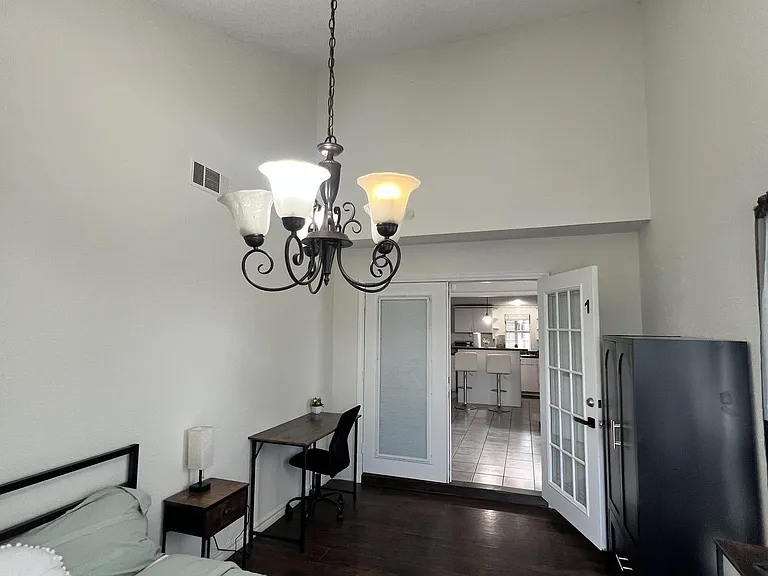 Private bedroom with high ceilings, wood floors, a study desk, dresser storage, and French-door access to common areas.