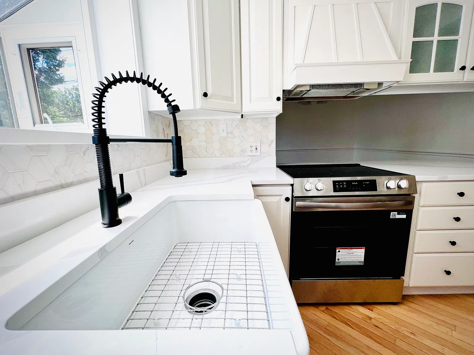 Newly updated kitchen featuring sleek quartz countertops, a classic white farmhouse sink with a high-arc gooseneck faucet, and brand-new electric appliances including an oven and dishwasher. Garden window to grow fresh herbs.