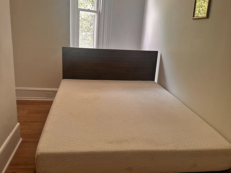 Streamlined bedroom with a platform bed, hardwood floors, and a tall window that brings in natural light.