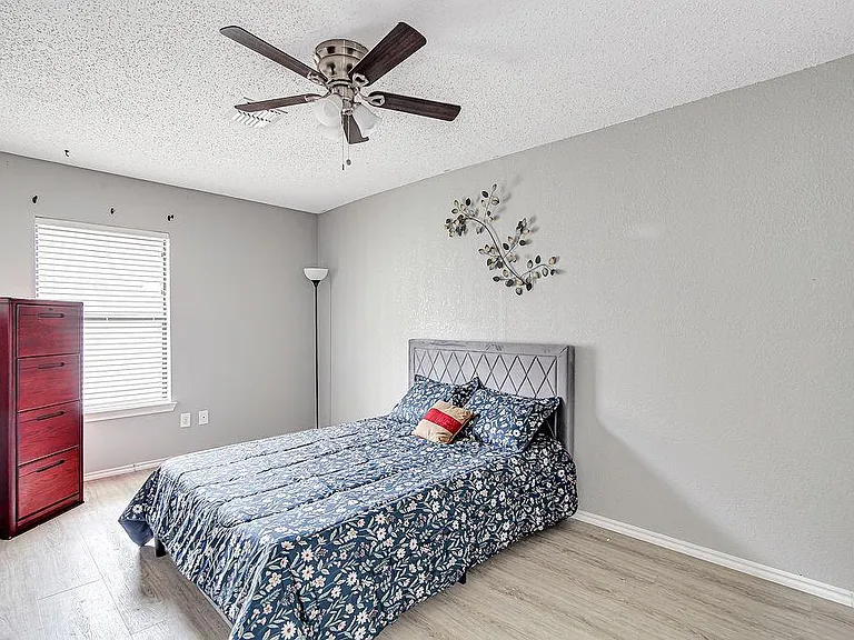 Furnished bedroom with a bed, dresser, ceiling fan, and window with blinds on easy-care flooring.