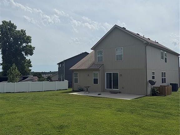 Expansive green lawn, white vinyl fencing, concrete patio, and sliding glass door access