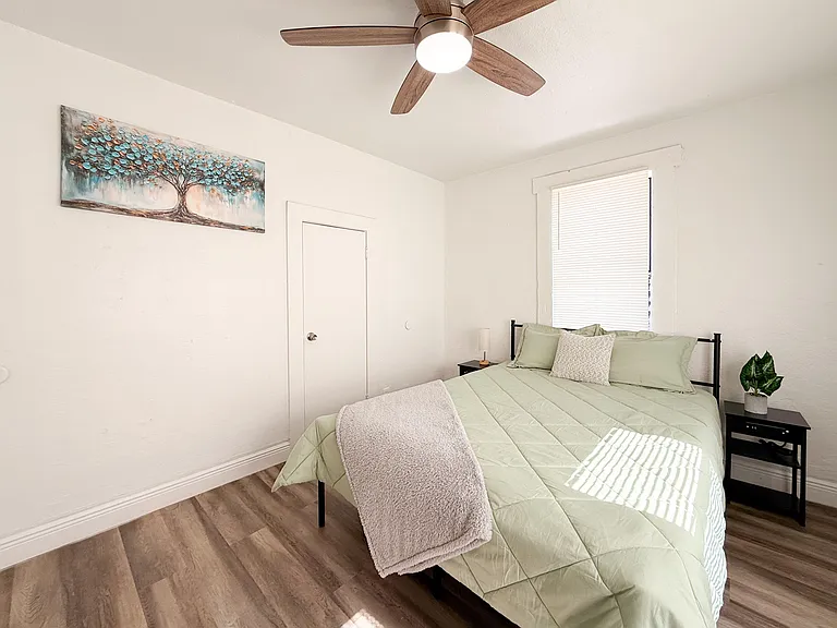 Furnished bedroom with a ceiling fan, window with blinds, and side tables for convenient bedside storage.