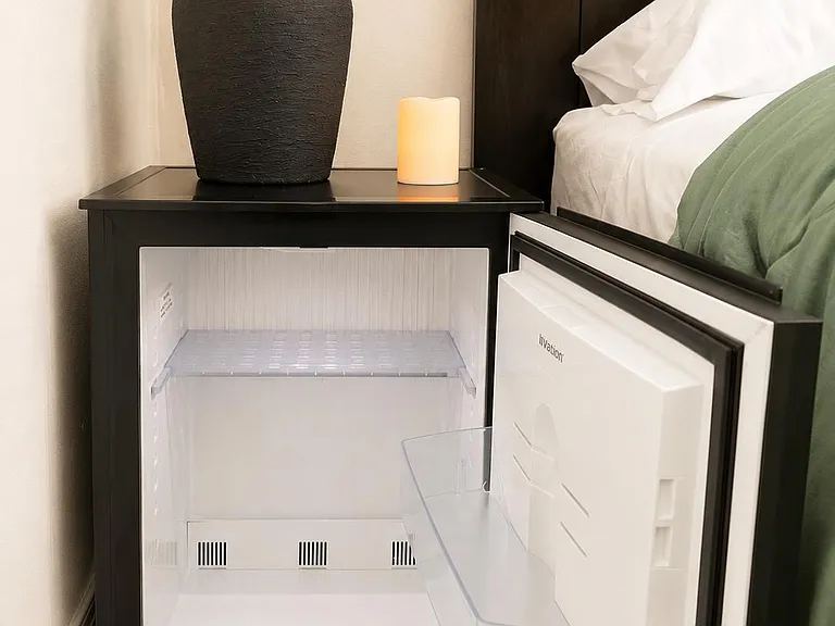 Bedroom setup includes a compact mini fridge beside the bed for convenient in-room snacks and drinks.