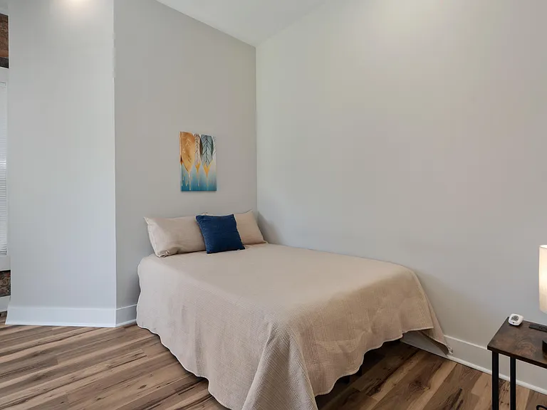 Full-sized bed, nightstand with lamp, and window blinds for light control.