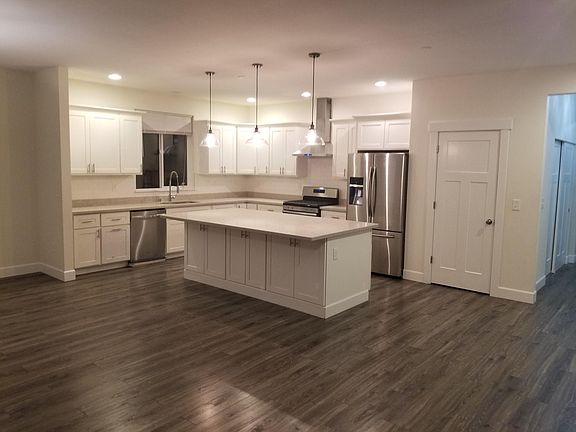 Kitchen with white cabinets, large island, stainless appliances, pantry and quartz countertops.