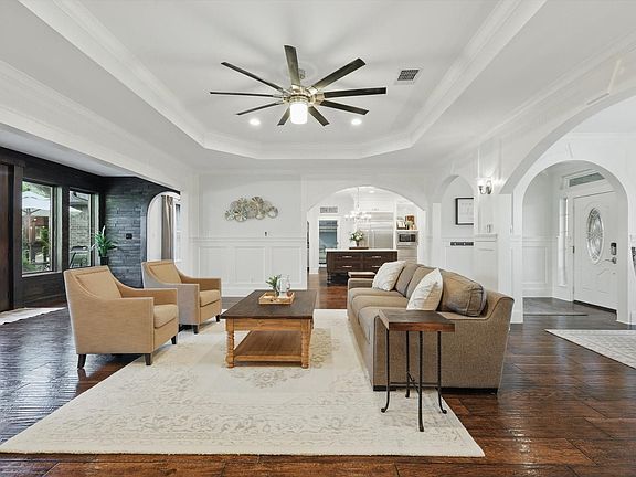 Living room with a decorative wall, arched walkways, a raised ceiling, crown molding, and ceiling fan