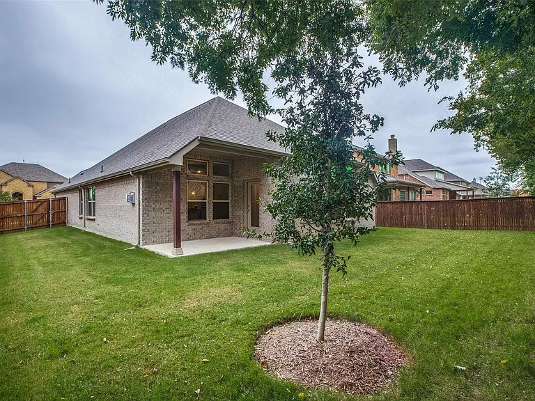 Expansive green lawn surrounds a covered patio, featuring a brick exterior and a privacy fence