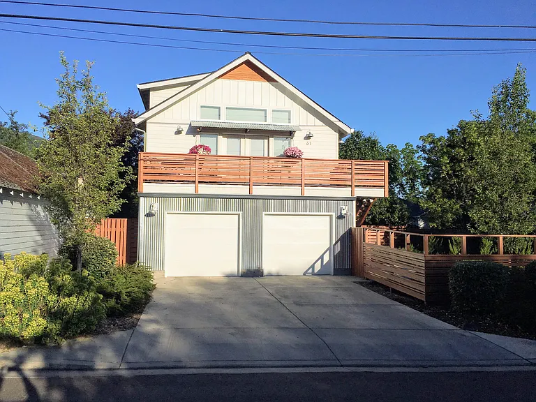Front of home with balcony and single car garage on right side. Entrance to home through gate on right.