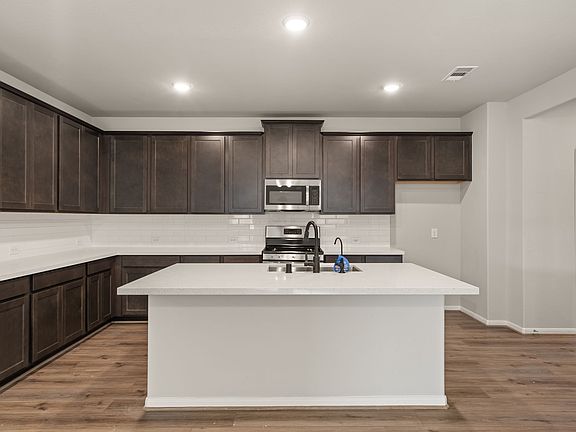 The kitchen featuring dark stained cabinetry, light quartz countertops and a modern tile backsplash