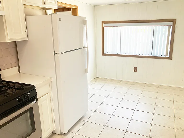 Kitchen, facing front of house -- breakfast area window. Door behind refrigerator leads to bedroom (converted garage).