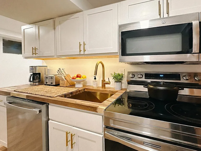 Updated kitchen with white cabinetry, stainless steel appliances, modern hardware, and warm wood-style flooring.
