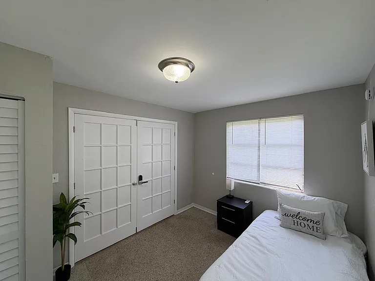Well-kept bedroom featuring French-door closet access, a large window with blinds, and space for a nightstand.