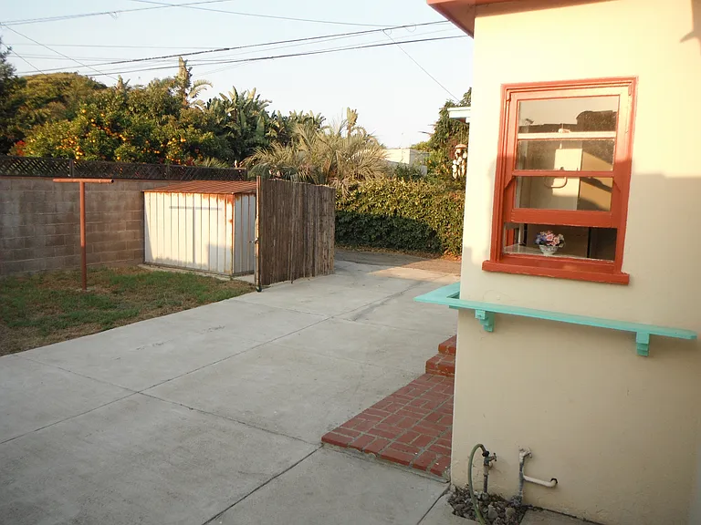 view toward alley entrance showing patio/parking area, storage shed, clothesline pole