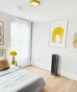 Well-sized bedroom with wood-look flooring, large window with curtains, and space for a full bed plus side table.