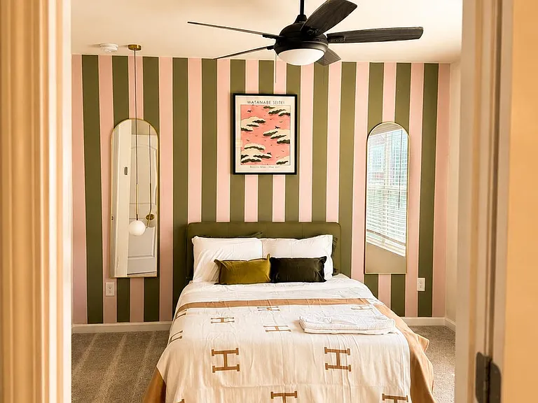 Furnished bedroom with a ceiling fan, accent wall, full-size bed, and a window with blinds for natural light.