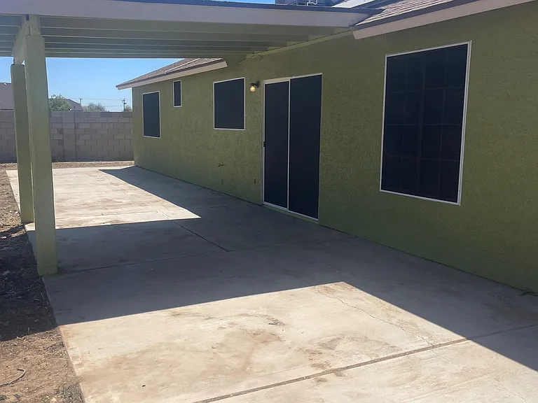 Covered backyard patio with a spacious concrete slab, exterior lighting, and access to the home through a sliding door.