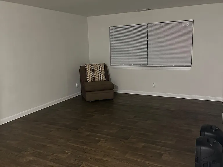 Spacious open room with durable wood-style flooring, neutral walls, and a large window with blinds for privacy.