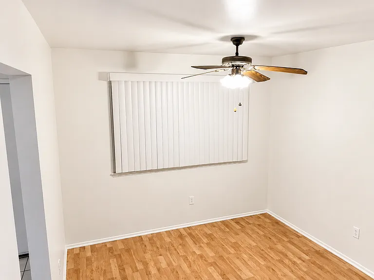 Bright dining area with wood-look flooring, ceiling fan, window coverings, and convenient access to the kitchen and main living space.